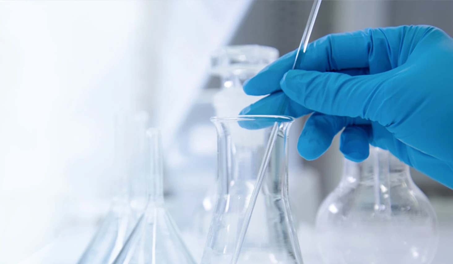 Mano con guanto protettivo usa una pipetta tra i contenitori di un laboratorio.